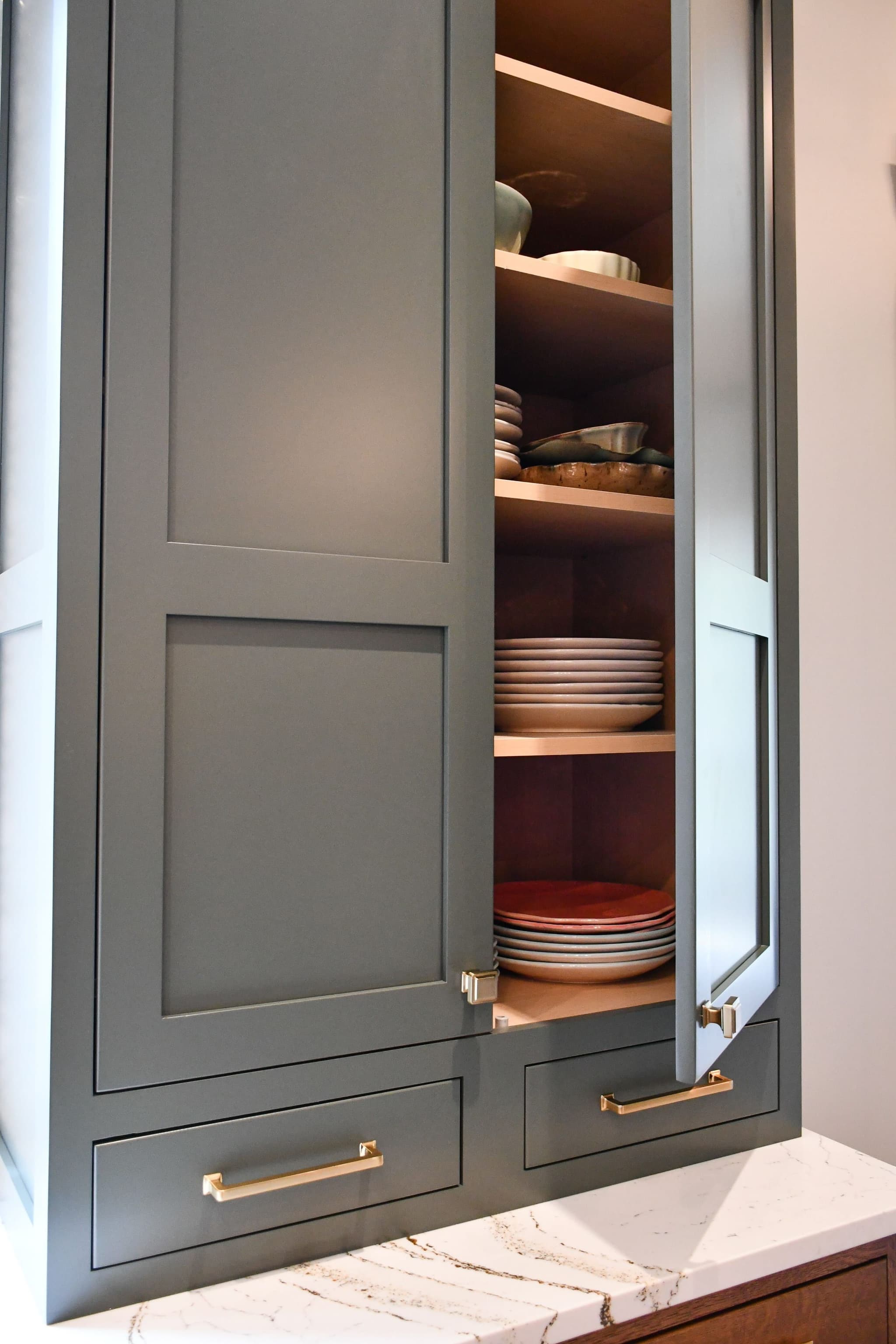 Gray-green kitchen cabinetry with brushed-gold pulls and open dish storage